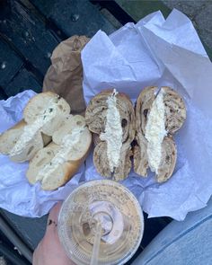 a person holding a drink next to two sandwiches on buns and paper napkins