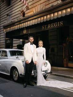 a man and woman in formal wear standing next to an old car on the street