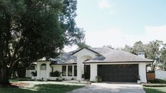 a white house with a black garage door and two trees in front of the house