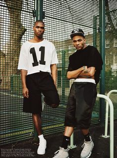 two young men standing next to each other in front of a fence and green gate