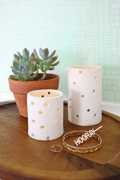 two white vases sitting on top of a wooden table next to a potted plant