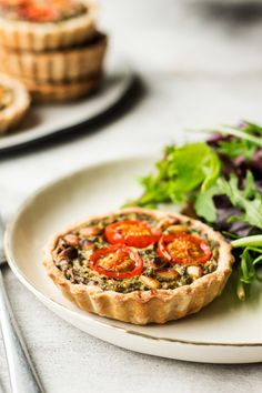 a small quiche with tomatoes and lettuce on a plate next to a salad