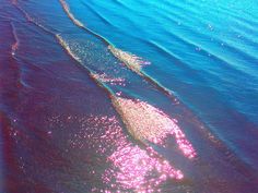 an aerial view of the ocean with pink and blue colors on the water's surface