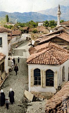 an old photo of people walking down a cobblestone street with buildings in the background