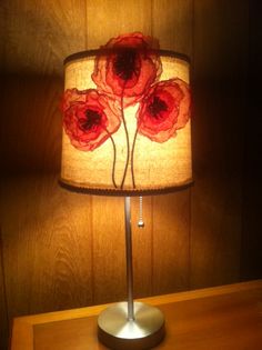 a lamp with red flowers on it sitting on a wooden table next to a wall