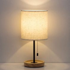 a table lamp with a wooden base and a white linen shade on the top of it