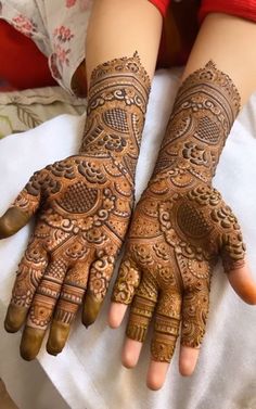 two hands with henna tattoos on them, one is showing off the intricate design