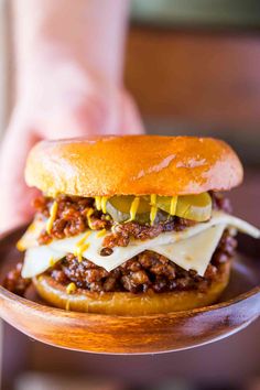 a chili cheeseburger on a wooden plate being held by a person's hand