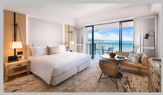 a hotel room with a bed, desk and chair in front of a balcony overlooking the ocean