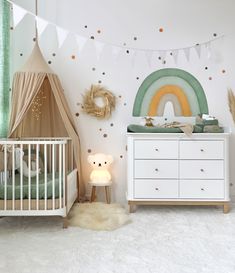 a baby's room with a crib, dresser and rainbow wall decal