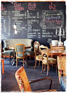 an old fashioned restaurant with tables and chairs in front of a chalkboard wall that has writing on it