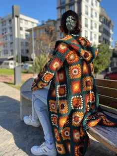 a woman sitting on a bench wearing a crocheted blanket