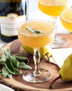 two glasses filled with pear cider and garnished with sage leaves on a wooden tray