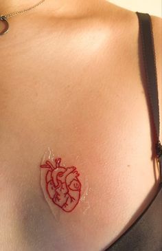 a woman's chest with a red heart tattoo on her left shoulder and right breast