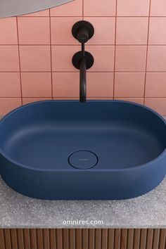 a round blue sink in a bathroom with pink tiles on the wall behind it and a black faucet