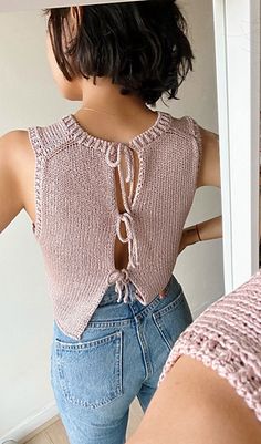 a woman is standing in front of a mirror wearing jeans and a pink top with laces on it