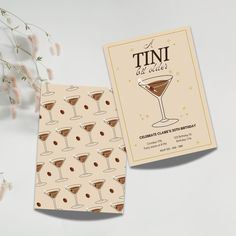 two business cards with martinis on them sitting next to some white flowers and branches