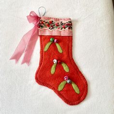 a red christmas stocking with green leaves and pink ribbon hanging on a white surface