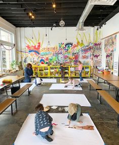 two children are sitting on the floor in front of some tables with white paper and paint