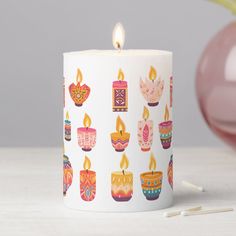 a white candle with colorful candles on it next to a pink vase and other items