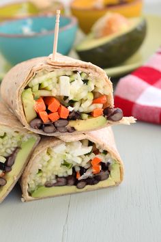 three burritos with vegetables and black beans are on a plate next to other food