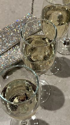 three glasses filled with white wine next to a silver purse on a gray tablecloth