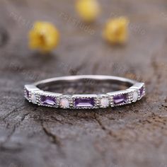 a white gold ring with amethyst stones and diamonds on the side, sitting on a piece of wood