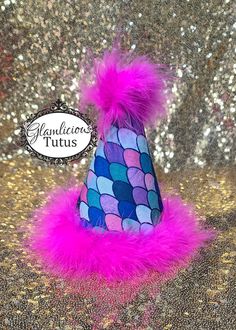 a purple and blue party hat with pink feathers on the top, against a gold glitter background