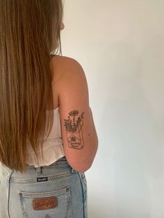 the back of a woman's shoulder with a tattoo on her left arm and flowers in a vase