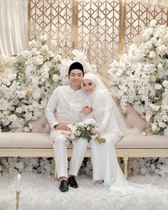 a man and woman sitting on a bench in front of white flowers, holding each other