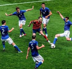 a group of men playing soccer against each other on a field with grass in front of them