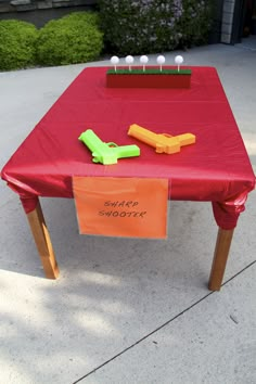 a red table topped with an orange and green plastic toy airplane next to a sign