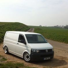 a white van parked on the side of a dirt road next to a green field