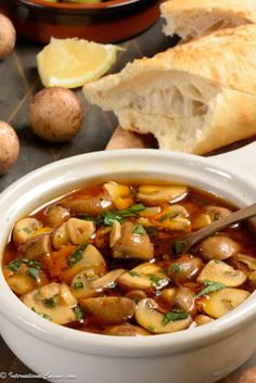 a white bowl filled with mushroom soup next to bread and lemon wedges on a table