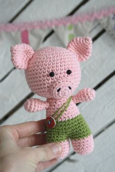 a small pink crocheted pig holding a green object in it's hand