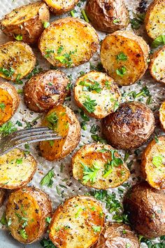 baked potatoes with parmesan cheese and herbs on a sheet of parchment paper next to a fork