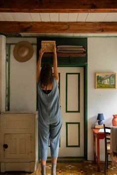 a woman in blue jumpsuits holding up a basket above her head while standing next to a door