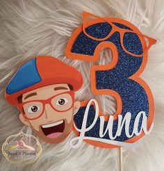 a birthday cake topper with the number three in blue glitter and an orange hat