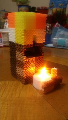 a lit candle sitting on top of a wooden table next to a lego block structure