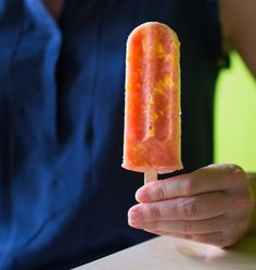 a person holding an orange and yellow popsicle on a stick in front of them