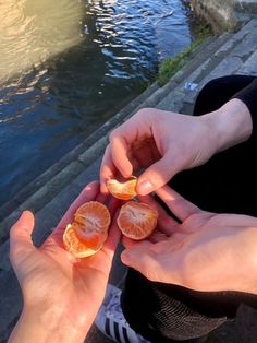 two people holding oranges in their hands by the water's edge, one is peeling it