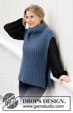 a woman leaning against a wall wearing a blue sweater