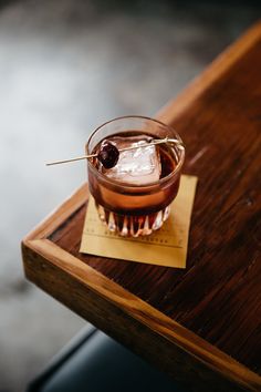 a drink with a garnish on the top sits on a wooden table next to a piece of paper