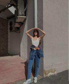 a woman standing next to a building with her hands on her head and arms behind her head