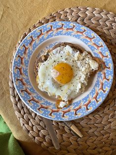 an egg is on top of toast in a blue and white plate next to a fork