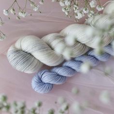 three skeins of yarn sitting on top of a pink surface next to white flowers