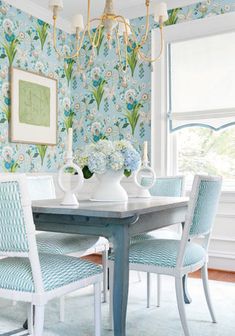 a dining room table with blue chairs and wallpaper on the walls in front of it