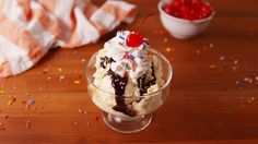 an ice cream sundae with cherries and sprinkles on a wooden table