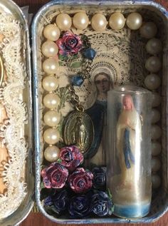 an open tin box with rosary, figurines and other items in it on a table