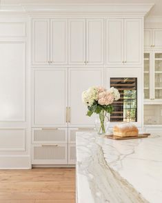 a kitchen with marble counter tops and white cabinets, along with flowers in a vase